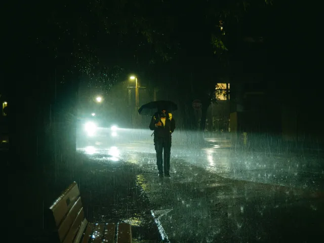 A pedestrian holds an umbrella while walking among puddles at night during a heavy rainstorm