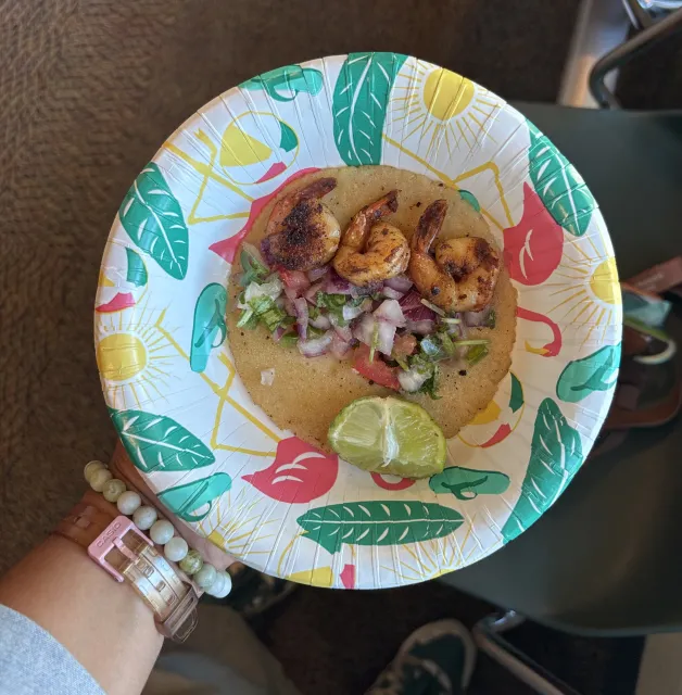 A shrimp taco on a colorful paper plate.