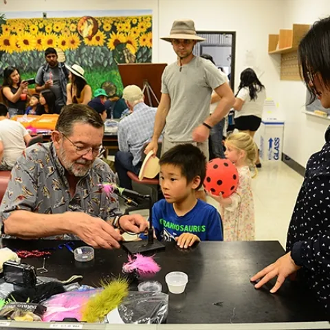 While mom (right) observes, Steven Mao, 7, of Davis, watches Dave Driscoll of the Fly Fishers of Davis tie a fly during the 104th annual UC Davis Picnic Day. (Photo by Kathy Keatley Garvey)