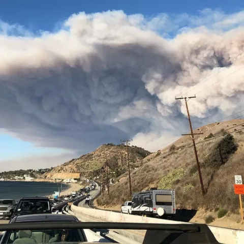 Traffic is backed up on Pacific Coast Highway as residents evacuate Malibu as a smoke plume from the Woolsey Fire rises in the background. (Photo: Wikimedia Commons)