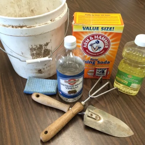 Baking soda, vinegar, vegetable oil, and a scrubber with garden tools.