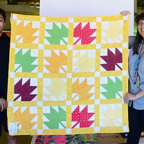 Gloria Gonzalez, superintendent of McCormack Hall at the Solano County Fair, holds a bee-themed quilt with assistant Jarod Fernander of Vallejo, 15, a student at the Pleasant Hill Adventist Academy. The quilt is the work of Tina Frothy of Vallejo. (Photo by Kathy Keatley Garvey)