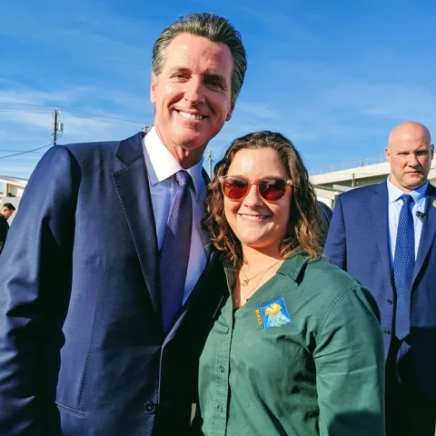 Gov. Newsom, wearing a dark suit, stands beside Katherine Uhde, who is wearing a green Master Gardener blouse.