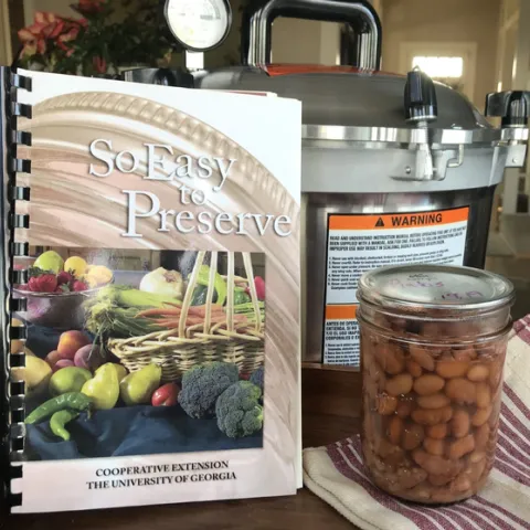 So Easy to Preserve recipe book, pressure canner, and finished jar of canned pinto beans