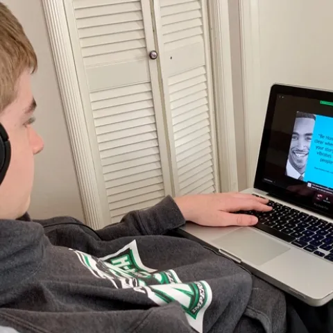 Youth with headphones looking at laptop screen showing a presentation