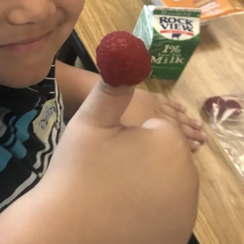 Child smiles and gives a thumbs up. There is a raspberry fixed onto the child's thumb.