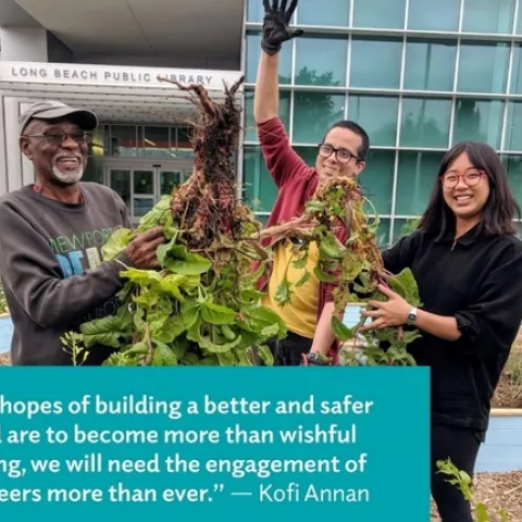 A diverse group of volunteers standing in front of the Long Beach Public Library holding a bunch of weeds.