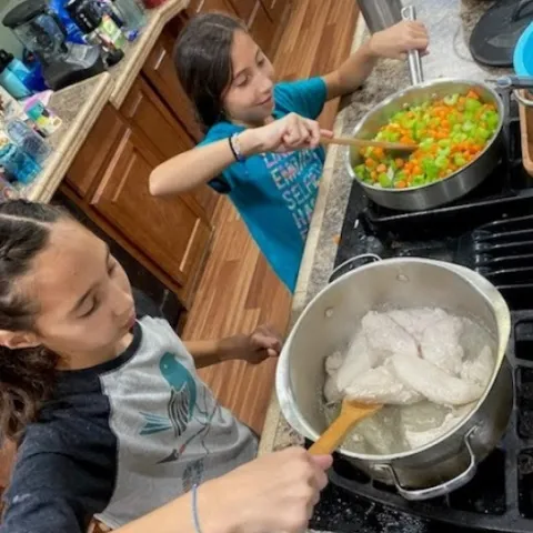 2 youth at stove stirring ingredients in 2 pots