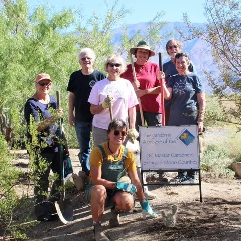 A group of people standing near a sign in a garden.