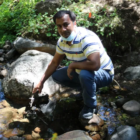 Safeez Khan crouches on stones as he samples water in a mountain stream.