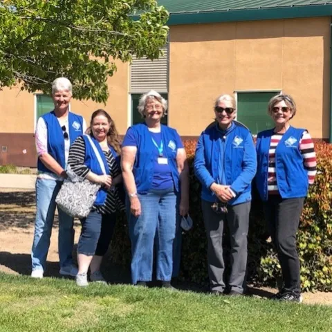 Five female master gardeners in blue vests stand in front of the Sensory Garden space.