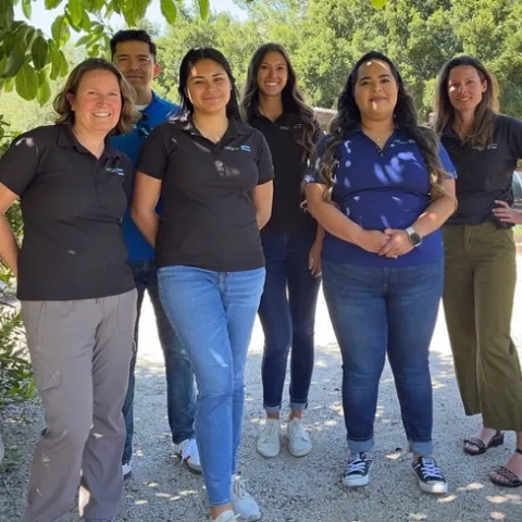 Miguel Diaz, Kelly Hong, Melissa LaFreniere, Abbi Marrs, Mishelle Petit, Rosa Vargas stand under a tree. Betsy Plascencia and Melissa Rorabough are missing from the picture.