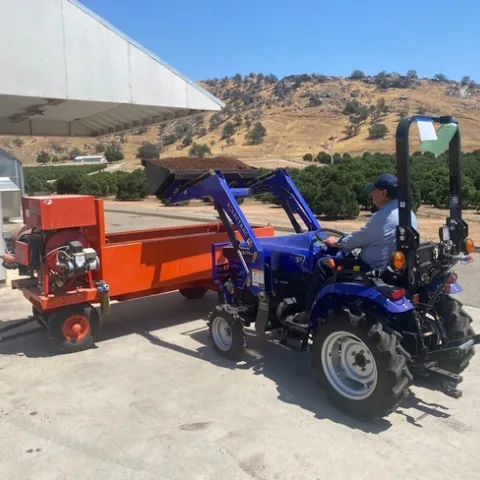 A blue tractor dumps soil into an orange bin for mixing.