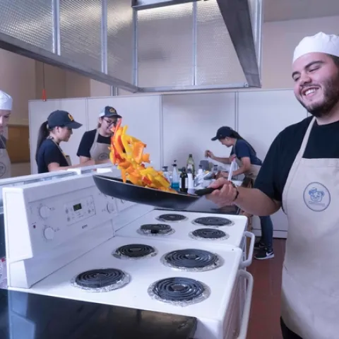 A student in the Cal Teaching Kitchen sautes bell peppers in a frying pan