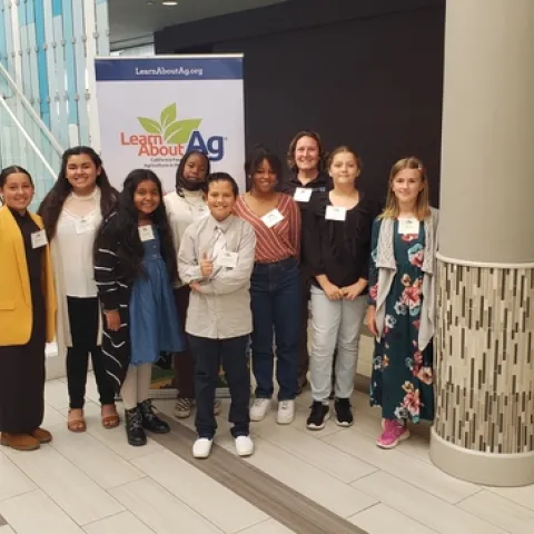 Several students stand and smile in front of a sign at the California Ag in the Classroom Conference