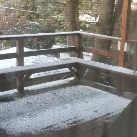 Looking out sliding glass doors to deck with two inches of snow on ground and railing