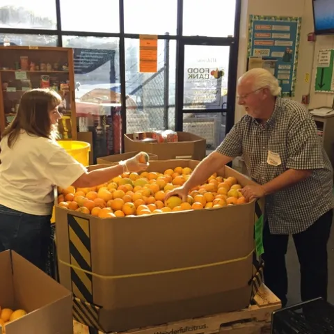 Dos voluntarios en el banco de alimentos preparando y separando naranjas.