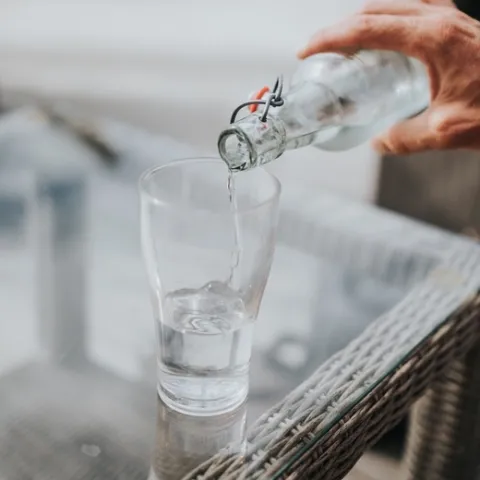 Water pours from a clear bottle into a drinking glass