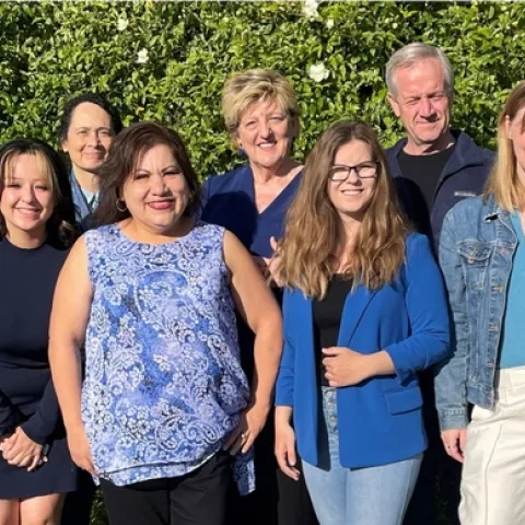 Seven people pose standing in front of flowering hedge