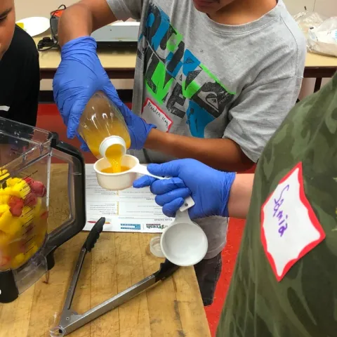 Un estudiante de Teens Love Cooking (Los adolescentes aman cocinar) miden ingredientes para hacer un batido.