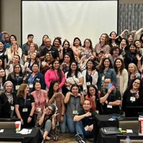 About 100 members of the Community Nutrition and Health network ham it up for a group photo in a conference room.
