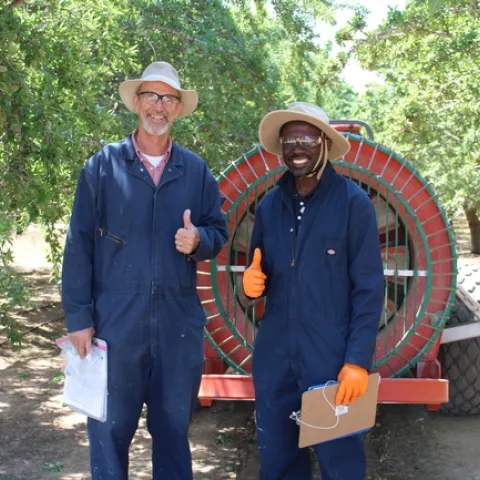 UCCE farm advisor Dr. Franz Niederholzer and UCCE specialist Dr. Peter Larbi pose behind an airblast sprayer in Arbuckle, CA