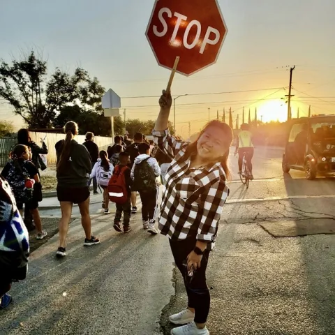 A woman holds a stop sign in a crosswalk as people walk and bike by