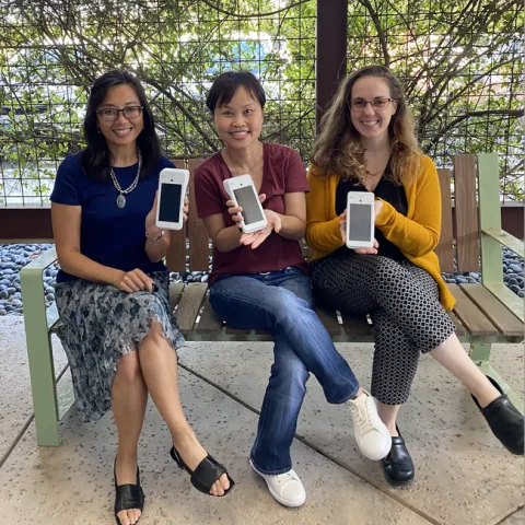 Three women sit holding credit card scanners that look like cell phones.