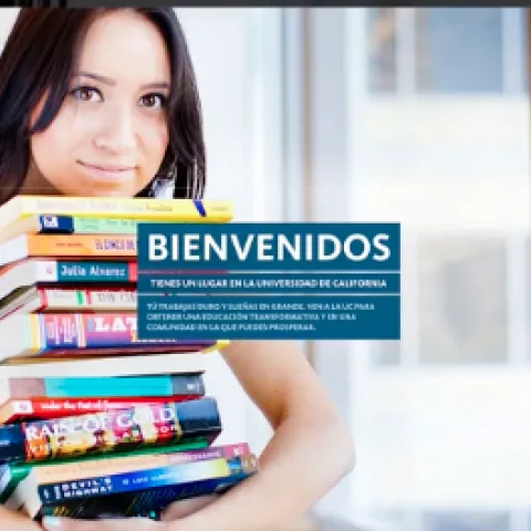 A dark-haired woman holds a stack of textbooks. Bienvenidos