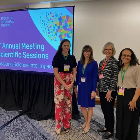 Four community health researchers stand by a screen at the Society of Behavioral Medicine Annual Meeting