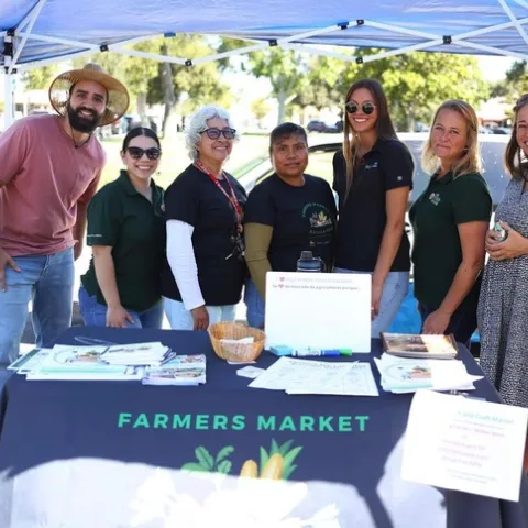 Seven people pose at a farmers market table