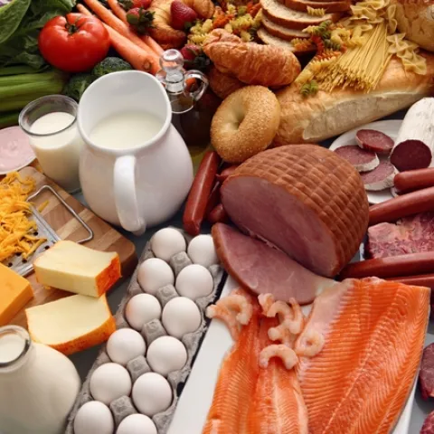 Assorted foods -- vegetables, milk, breads, cheese, eggs, ham, salmon -- on a table.