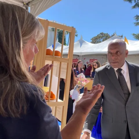 Tammy stands behind the booth table and Bradford picks up an avocado