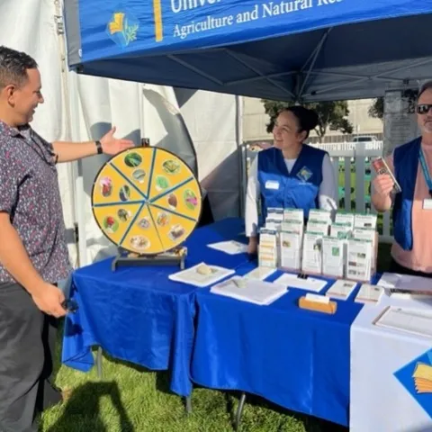 Two smiling Master Gardeners wearing vests help someone answer questions.