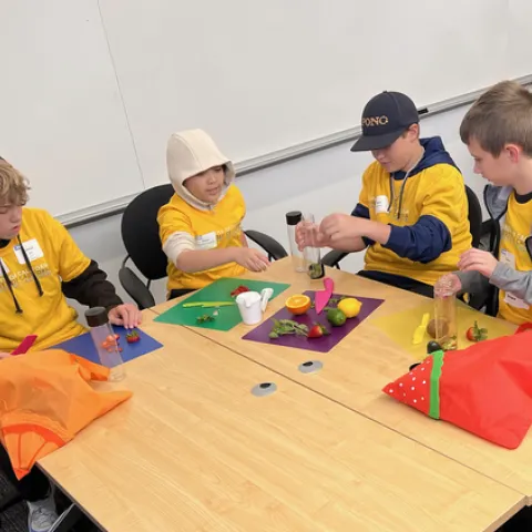 Four kids in yellow UC shirts slice citrus and berries to put in reusable bottles.