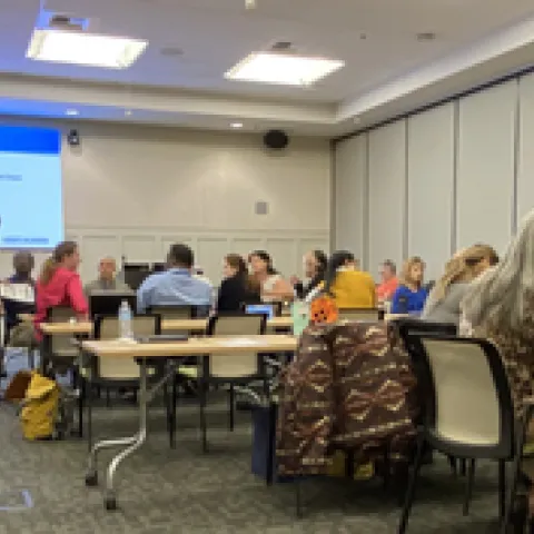 Dozens of people sit at conference room tables. PowerPoint screen reads: "Turn the Table" Discussion. Ask your BP Team questions. Jepardy topics: Procurement, T&E, C&G, Fiscal Close. Choose 2-3 topics, discuss a pain point, effciency and kudo.