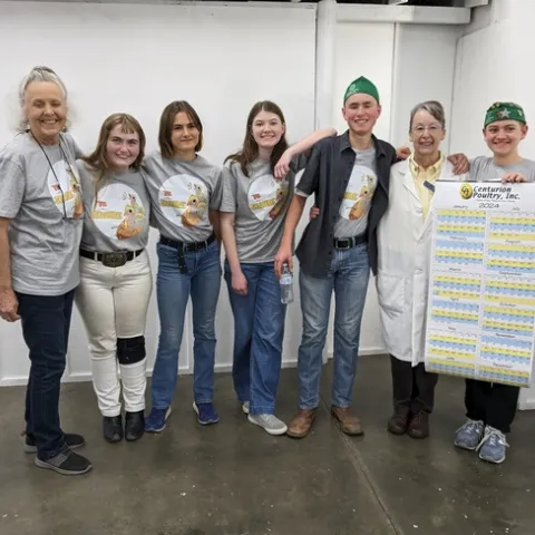 2 adults stand with 5 youth holding a large calendar poster