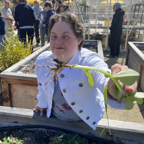 Uno de los participantes del programa MORE sostiene una raíz de haba para mostrar sus nódulos de nitrógeno, durante su visita al huerto del campus. Fotografía por Tracy Celio