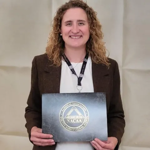 Laura Snell holds a plaque with the logo of the National Association of County Agricultural Agents.