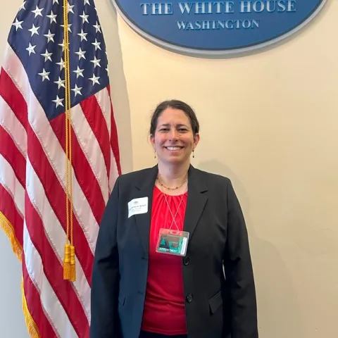 Ruth Dahlquist-Willard standing next to the American flag under a blue sign that reads "The White House, Washington."
