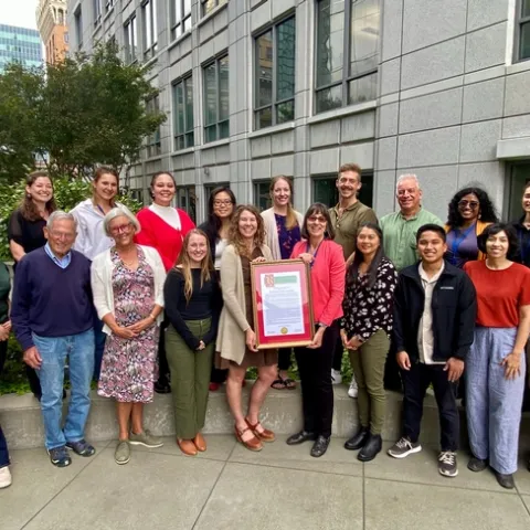 Nineteen members of the Nutrition Policy Institute flank the framed resolution in the roof garden of UC Office of the President in Oakland.