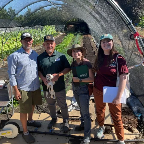 Four people stand in front of a hoop house