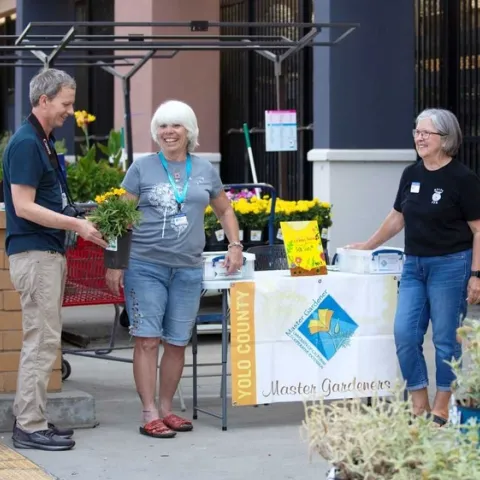 People talking in front of a UC Master Gardener Table at a garden store