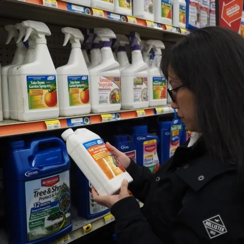 A dark haired woman holds a pesticide bottle in her hand to read it.