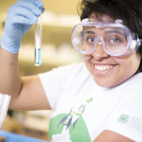 Youth wearing safety goggles and gloves holding text tubes of liquid