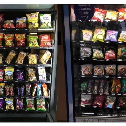 Two vending machines side by side. The one on the left contains less healthy processed food items, and the one on the right contains healthier food items and snacks.