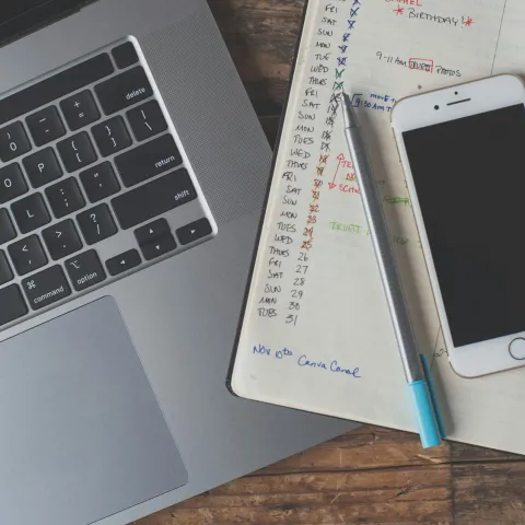 A laptop, notebook, and cellphone on a desk