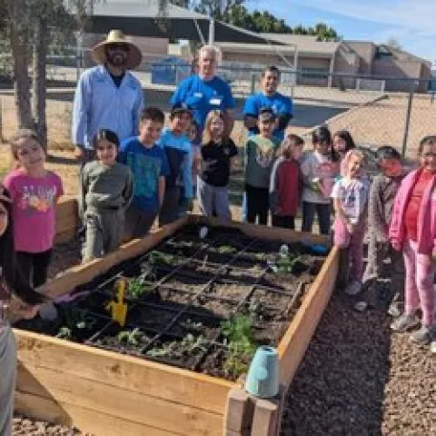 UCMGs and little students around a wooden raised garden bed.