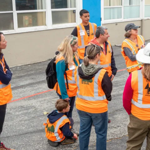 A group of volunteers wearing orange and yellow vests gather in a circle