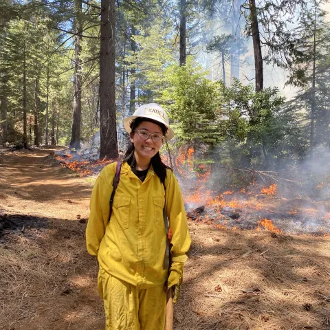 Katie Low stands by a prescribed fire in a forest setting